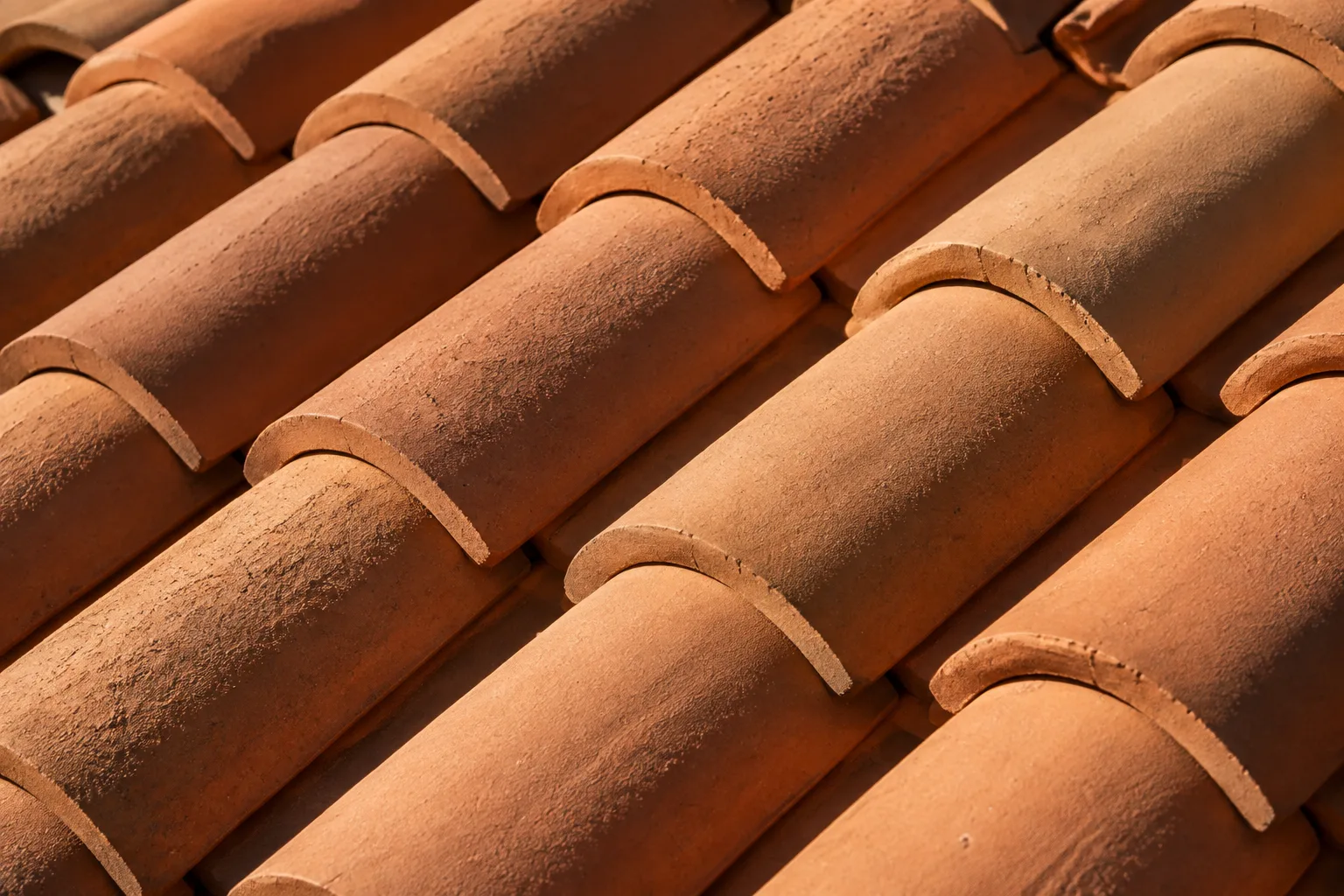 Illustrative close-up of terracotta barrel tiles, showing the clay texture, curved edges and shadows between courses
