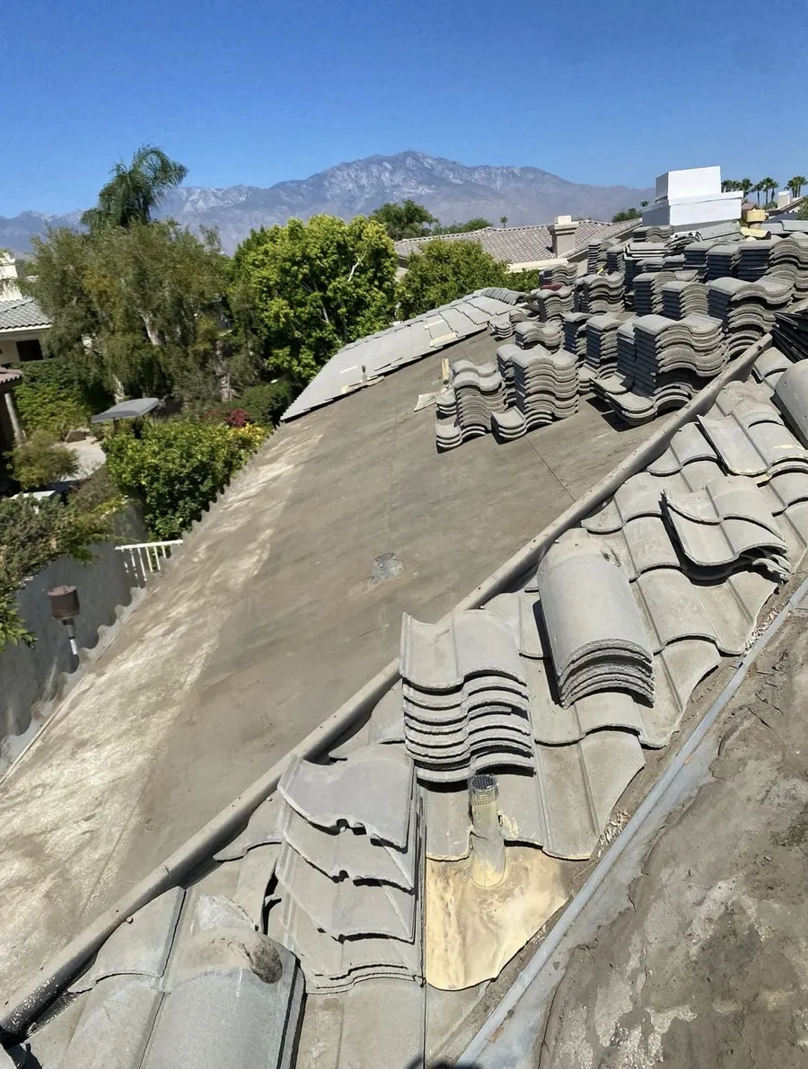 Barrel tiles lifted and stacked in rows across a roof while the deck beneath is worked on