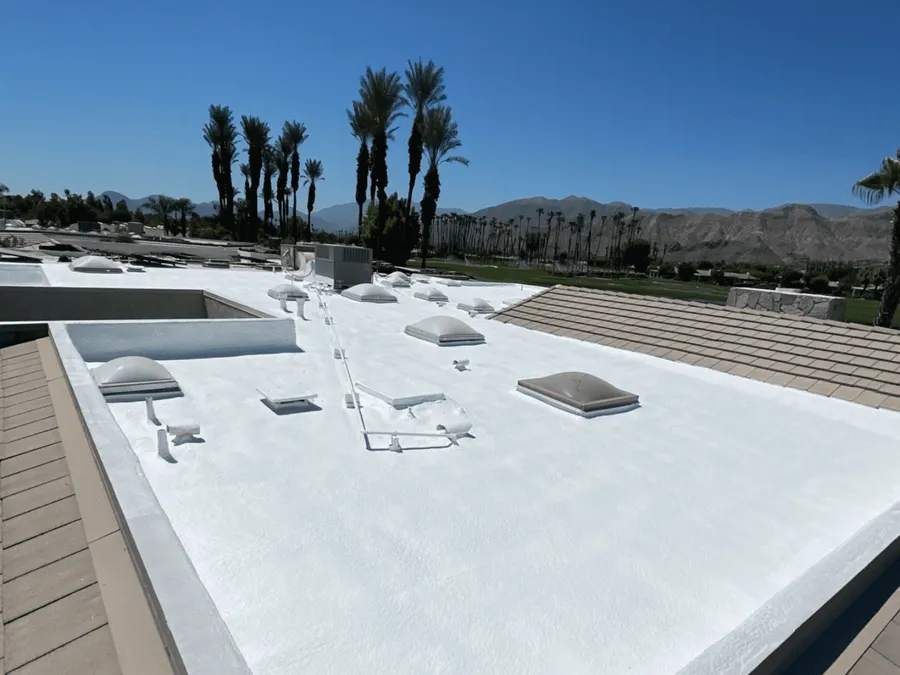 A white spray foam roof deck with curbs and skylights, a tile roof adjoining it and mountains behind