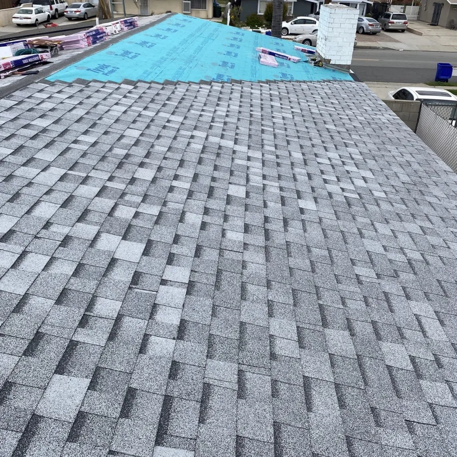 A grey shingle roof part-laid, blue underlayment and bundles of shingles still up at the ridge